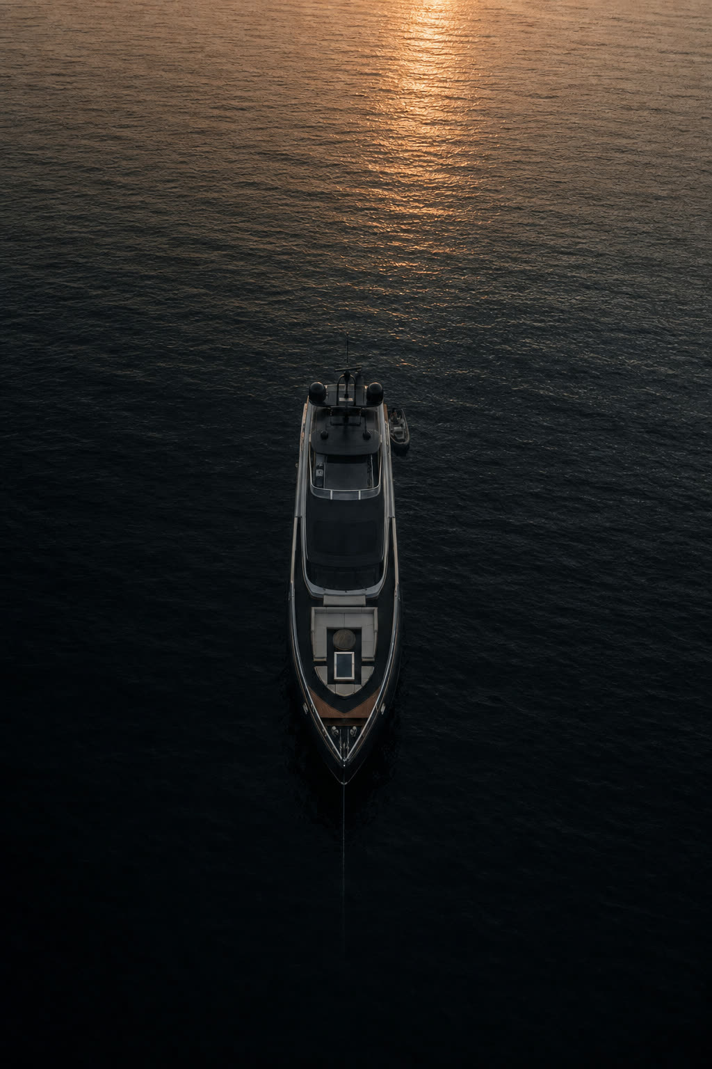 Aerial view of a dark-hulled yacht anchored in calm open water at dusk