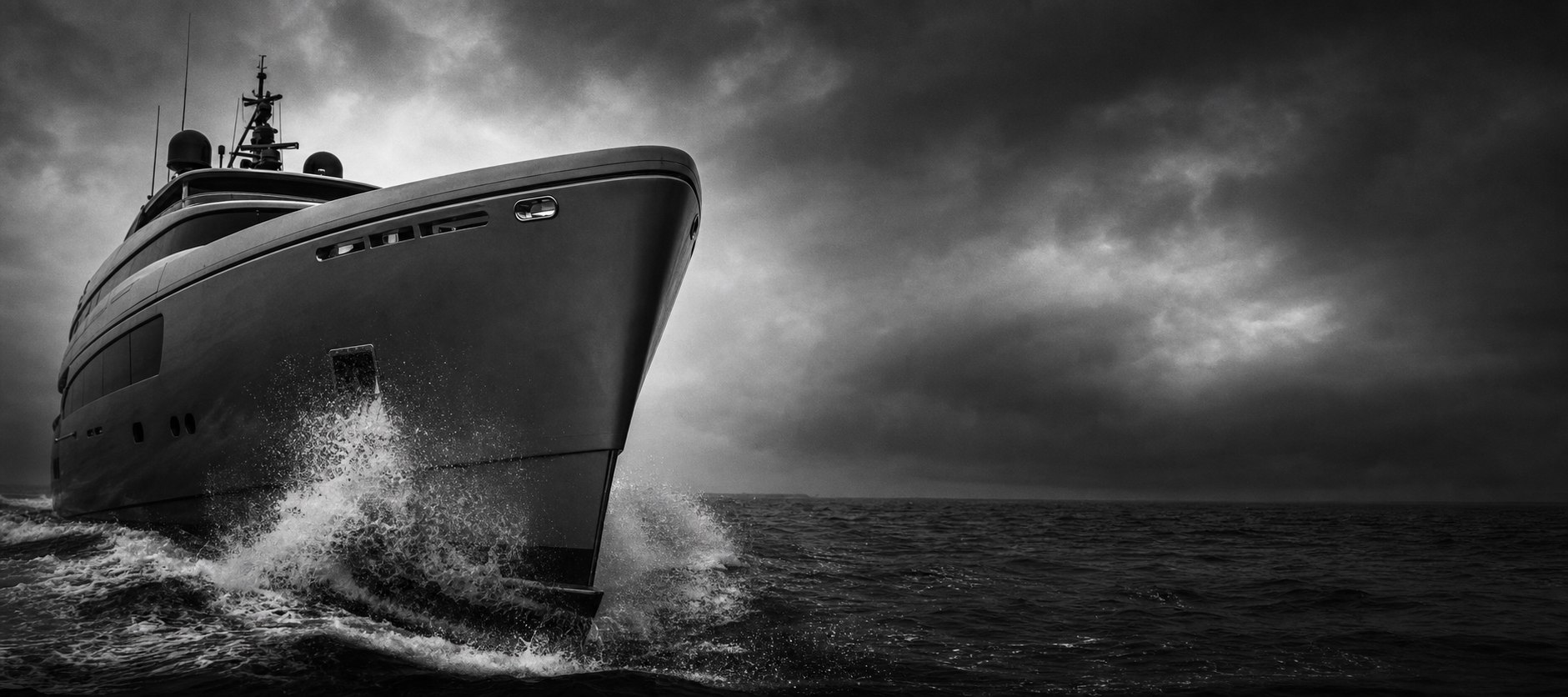 Close low-angle view of a superyacht bow cutting through dark water under a dramatic monochrome sky